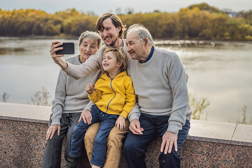 Senior couple with grandson and great-grandson take a selfie in the autumn park. Great-grandmother, great-grandfather and great-grandson.
