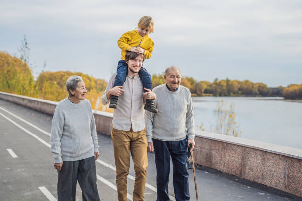 an elderly couple walks in the park with a river with their grandson and great-grandson - 11892 - fotografias e filmes do acervo