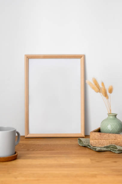 istock A frame with a blank canvas against a light wall and on a wooden tabletop with vase and cup of tea. 1966726353