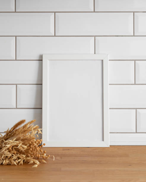istock A  frame with a blank canvas against a white tile wall and on a wooden tabletop with dry bouquet. 1966730544