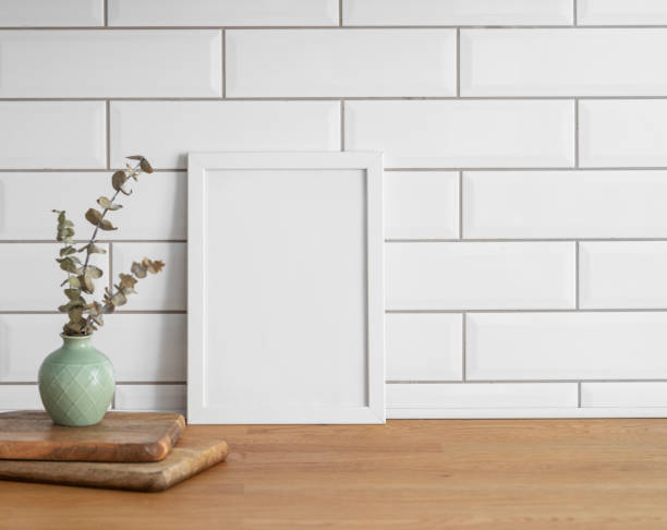 istock A  frame with a blank canvas against a white tile wall and on a wooden tabletop with vase. 1966730546