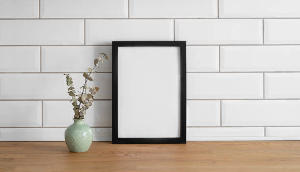 istock A  frame with a blank canvas against a white tile wall and on a wooden tabletop with vase 1966730549