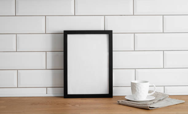 istock A  frame with a blank canvas against a white tile wall and on a wooden tabletop with cup of tea. 1966731082
