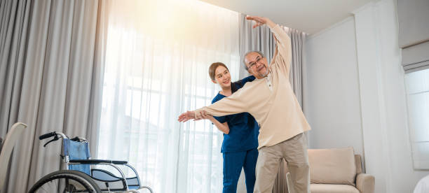 istock Old senior man enjoys training with physiotherapist for outstretched arms at home 1966774300