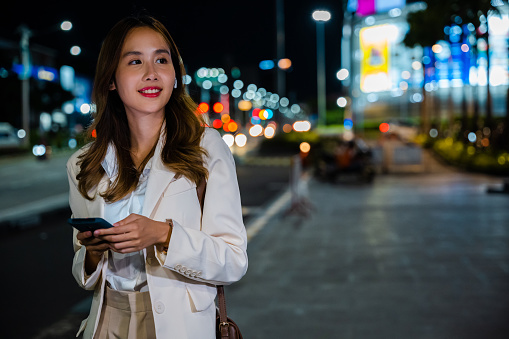 Stylish blogger woman walking in autumn city streets and texting on smartphone at night. Urban technology lifestyle concept.