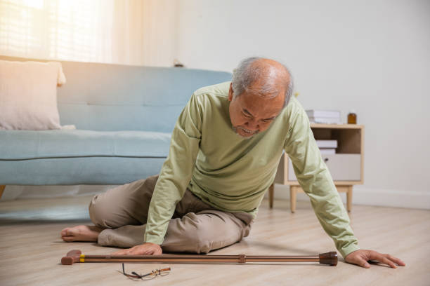 Asian senior man falling down lying on floor at home alone with wooden walking stick - foto de acervo