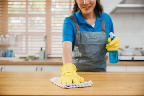 istock Focused Asian woman in yellow gloves cleans kitchen counter using liquid spray and rag. Housekeeping service ensuring cleanliness at home. Clean disinfect home care. maid household job. 1966793928