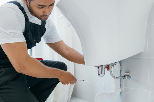 A skilled plumber uses a wrench fixing a water pipe under a bathroom sink. His repair service emphasizes plumbing maintenance clogged pipeline cleaning and rust removal for improvement.