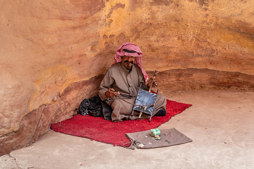 Wadi Musa, Jordan, October 05, 2023 : A Bedouin sits on mat and plays Bedouin one stringed lute for tourists in Al Siq gorge in the Nabataean kingdom of Petra in the Wadi Musa city in Jordan