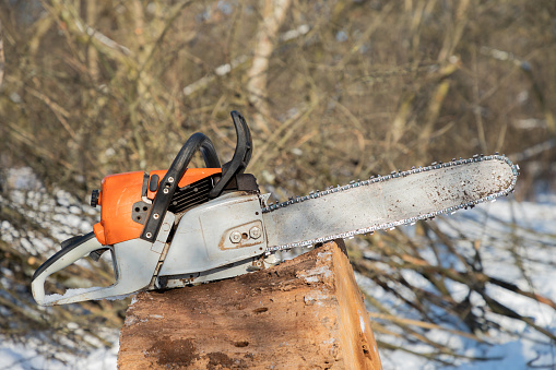 Petrol or electric battery powered chainsaw. Chainsaw on wooden stump or firewood. Firewood processing. Close-up.