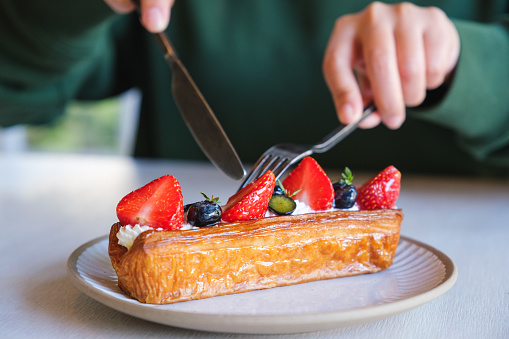 Closeup image of a woman eating a piece of mix berry log croissant with knife and fork