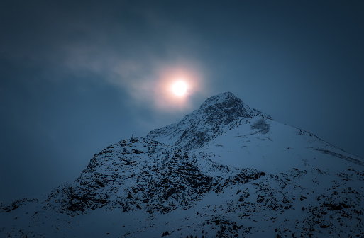 The Full moon rising above a slender snow-capped mountain in the breathtaking snowy range, Tyrol, Austria