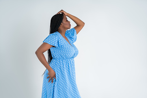 Plus size female model posing in blue dress on white studio background, young African woman with curvy figure and pigtailed hairstyle, afro braids