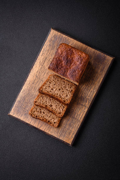 Delicious fresh crispy brown bread with seeds and grains on a dark concrete background