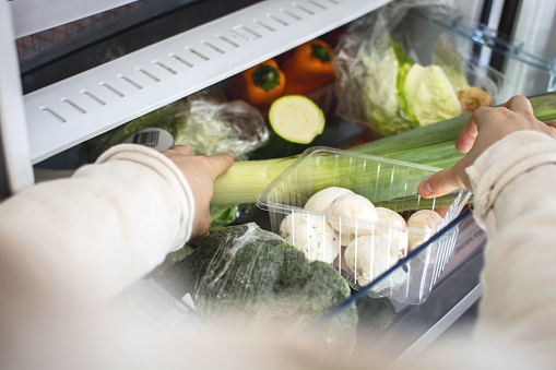 First-person point of view (POV) shot of a person opening and reaching in to a fridge draw, filled with a selection of healthy vegetables, including leeks, broccoli, peppers and mushrooms