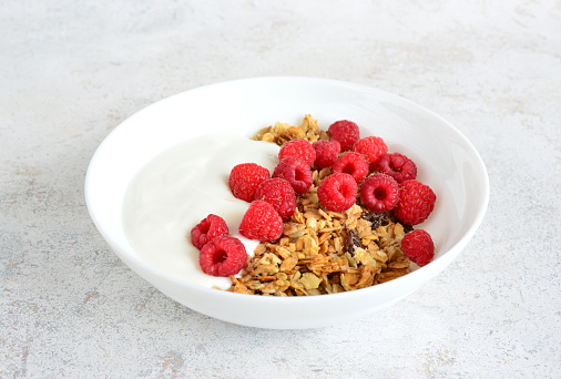 muesli with yoghurt and fresh raspberries in bowl close up
