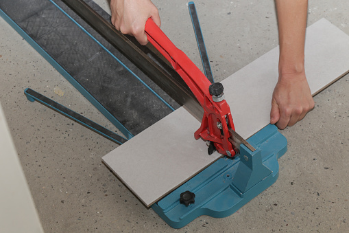 Cutingt tiles with a standard manual tile cutter. Process of installation of tiles in the bathroom step by step. DIY home improvement.