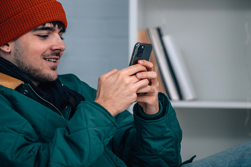 young man at home with mobile phone wearing warm or winter clothes