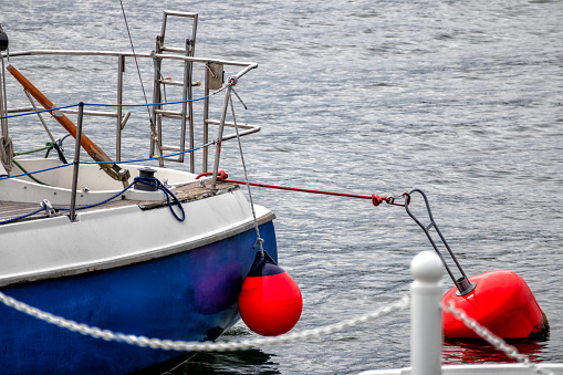 A red buoy in the water with the stern of a blue cutter moored on the shore