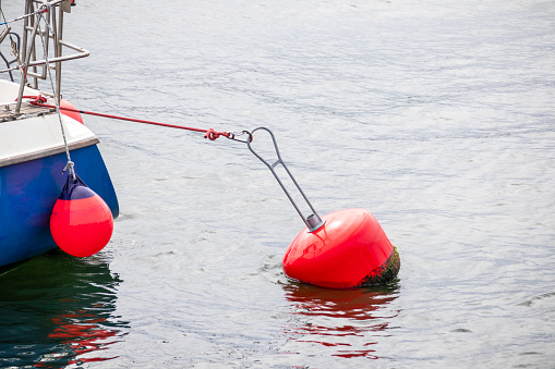 A red buoy in the water with the stern of a blue cutter moored on the shore