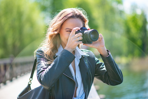 Woman using her digital camera in a park near a lake