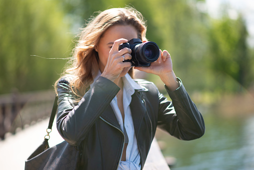 Woman using her digital camera in a park near a lake
