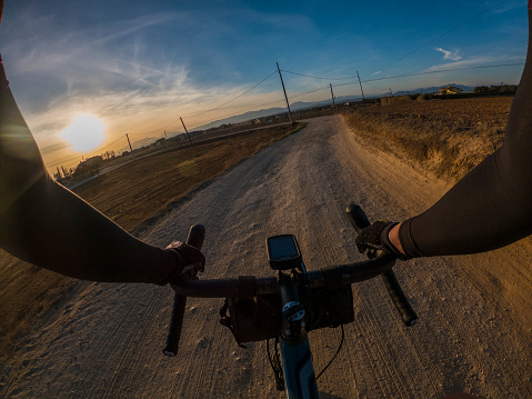 Riding a gravel bike on a dusty track on a sunset landscape rider point of view