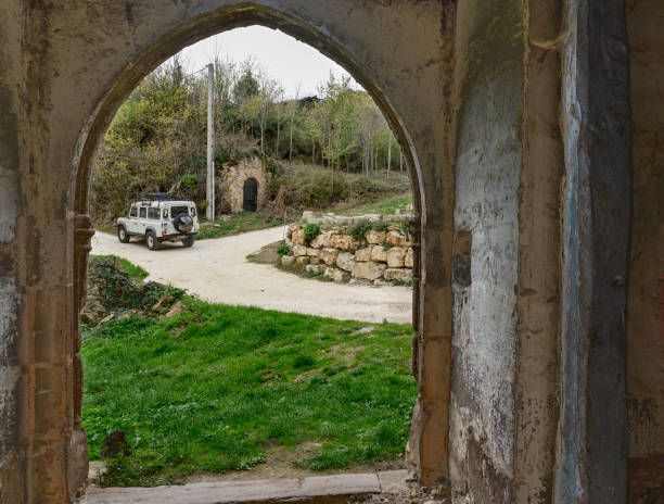 "스페인 부르고스 (burgos)의 한 마을의 돌담 옆 거리에 주차 된 흰색 랜드 로버 디펜더 (land rover defender)의 넓은 중세 아치 모양의 문을 통해 버려진 교회의 내부에서 바라 본 모습." - gothic style road car spooky 뉴스 사진 이미지