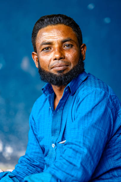 A Man from Dhaka Bangladesh is posing for a portrait in front of a blue background