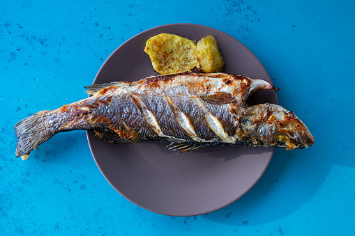 Oven-fried sea bass on a plate with a side of potatoes.