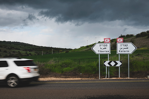 On the north shore of Israel's Lake Tiberias (Sea of Galilee) at Tabgha, a car passes signs pointing the directions to Tiberias and Katsrin. (January 27, 2024)