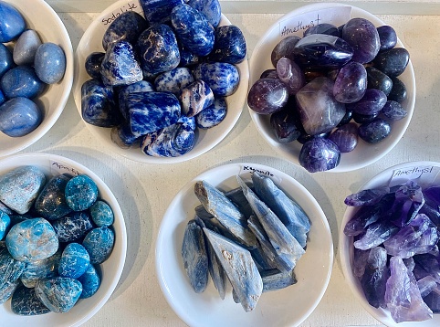 Horizontal flat lay of white ceramic bowls of small raw crystal stones in blue and purple tones, of amethyst, kyonite, sodalite & more  in Byron Bay Australia