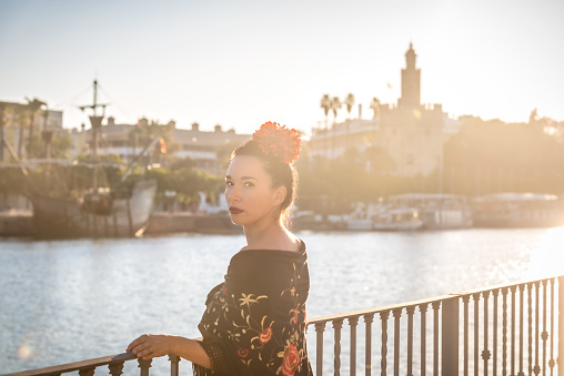 Morning view of a woman with Manton de manila (Manila Shawl) in front of Torre del Oro in Seville and a red flower in his head