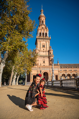 happy tourist mother and daughter enjoying Spain dressed with red flamenco costume in front of the Torre del Oro, Seville, Spain