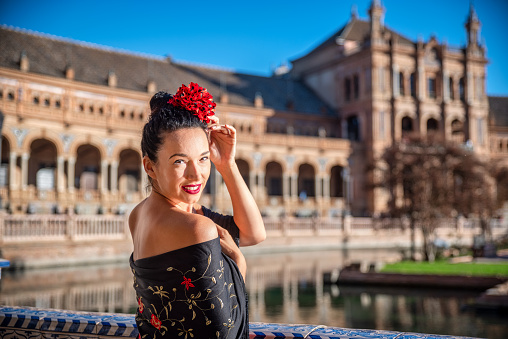 Beautiful woman in flamenco costume and a red rose in his head enjoying a day in Plaza de España in Seville. Spain