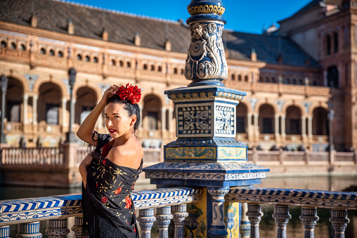 Beautiful woman in flamenco costume and a red rose in his head enjoying a day in Plaza de España in Seville. Spain