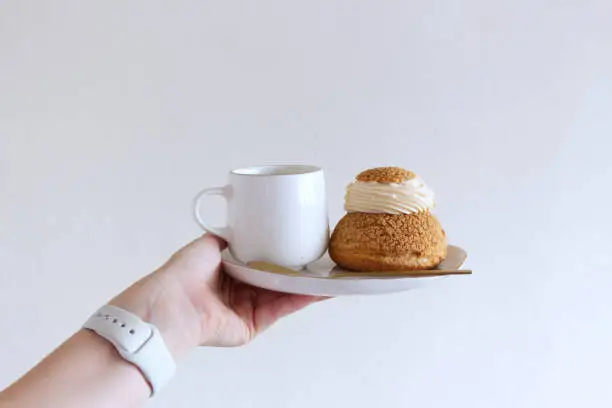 Tasty coffee and craquelin choux pastry cream-puff dessert filled with cream on a plate. Food concept.