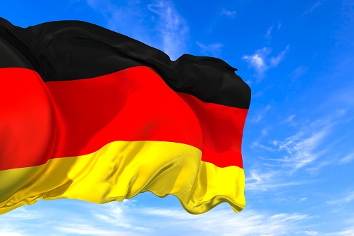 The national flag of Germany with fabric texture waving in the wind on a blue sky. 3D Illustration