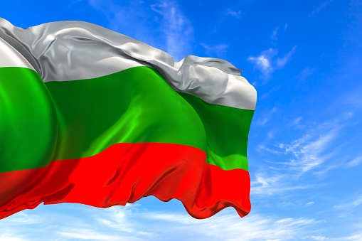 The national flag of Bulgaria with fabric texture waving in the wind on a blue sky. 3D Illustration