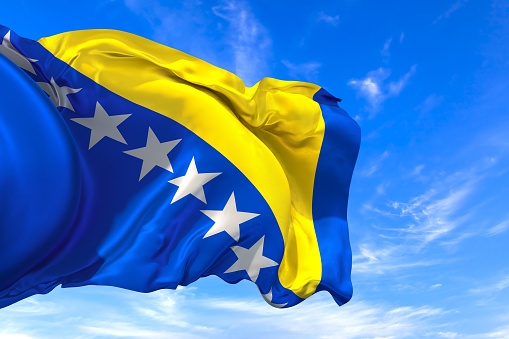 The national flag of Bosnia and Herzegovina with fabric texture waving in the wind on a blue sky. 3D Illustration