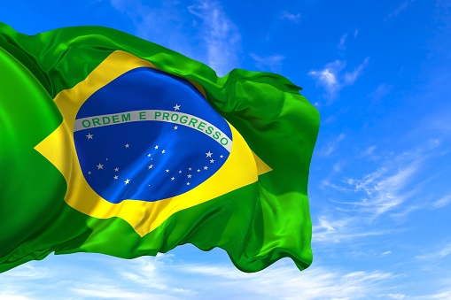 The national flag of Brazil with fabric texture waving in the wind on a blue sky. 3D Illustration