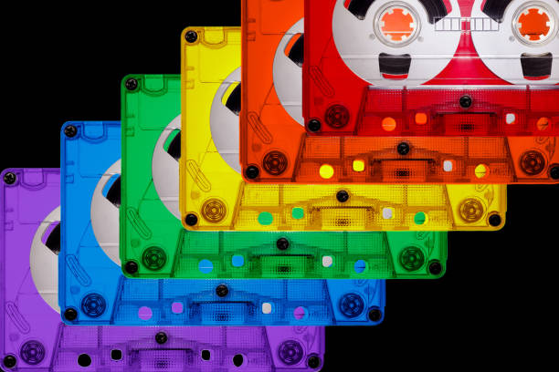 Colored transparent plastic compact audio cassettes lined up in a row on a black background. Bright colors of the LGBT rainbow. The picture is suitable as a background for the music theme