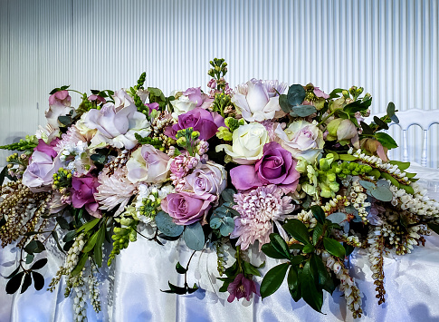 Large floral bouquet occupies the front of a bridal table. Fresh seasonal multi-colored flowers and leaves skilfully arranged in close proximity.