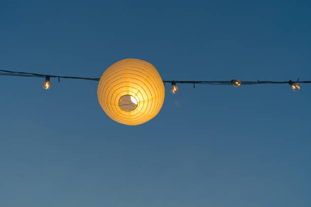 A paper lantern hanging from a wire against a clear blue sky backdrop.