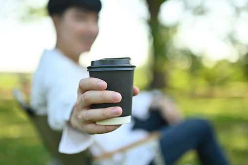 Close-up image of unrecognizable hand giving takeaway coffee cup, Park, and outdoor.