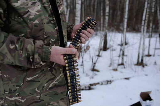 long machine gun tape, in the hands of a man in military uniform, standing in a winter forest.