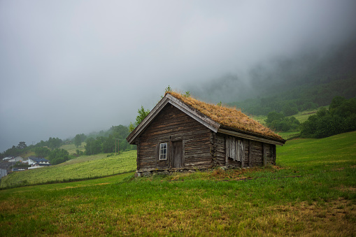 An abandoned cabin with a living roof stands on a hill in Loen, Norway during a cloudy, overcast day.