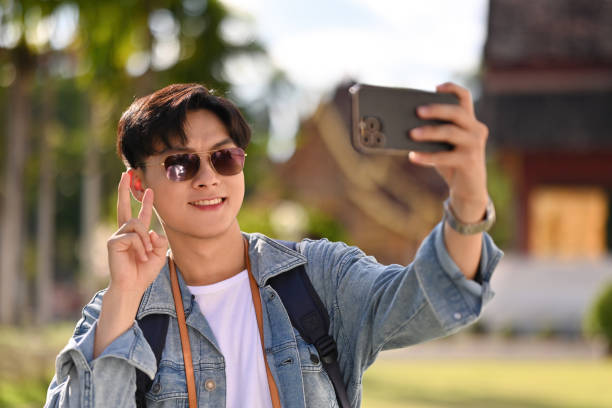 A handsome Asian tourist man with sunglasses taking a selfie while visiting a Thai Temple, Solo traveler concept