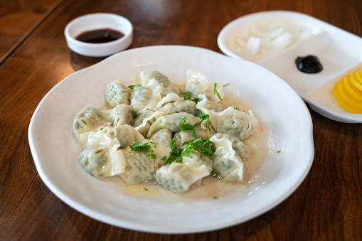 Fresh, delicious boiled garlic chives dumplings with green onions, jiaozi in white plate on wooden table background.