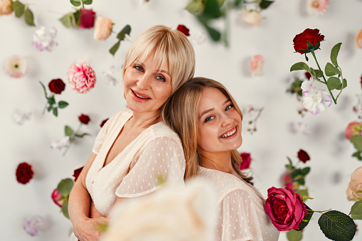 Happy Mother's Day and Women's Day. Mom and daughter in dresses standing hugging isolated on a white background, there are many flowers in the air around.